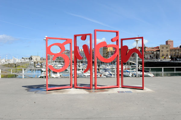 roter Eisen-Schriftzug der Stadt Gijón am Wasser der asturischen Metropole in Spanien