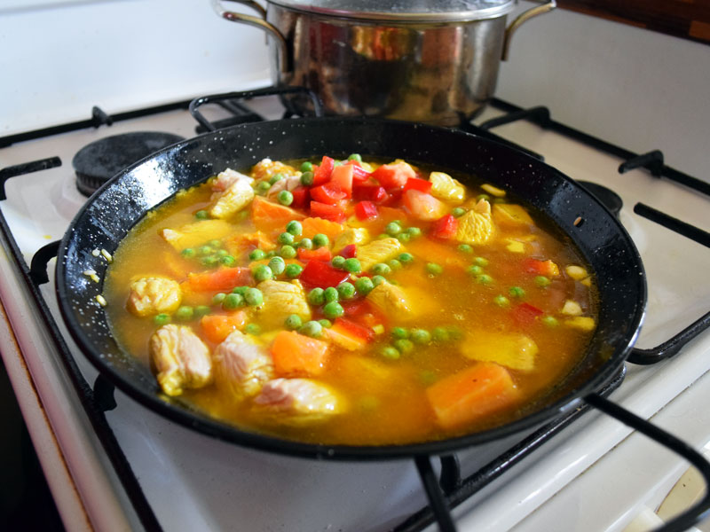Nun kommen Erbsen und Paprikawürfel in die Paella