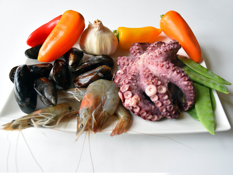 Paella-Zutaten: Pulpo, Miesmuscheln, Paprika, Garnelen, Knolauch und Meeresfrüchte